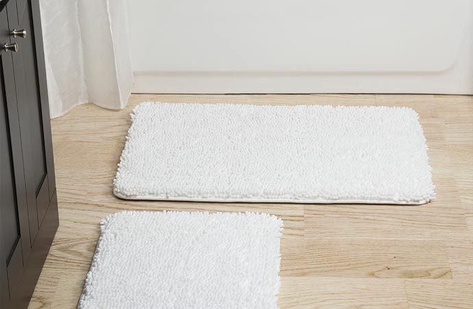 Add charm to your bathroom with a white cotton bath mat on a wooden floor.